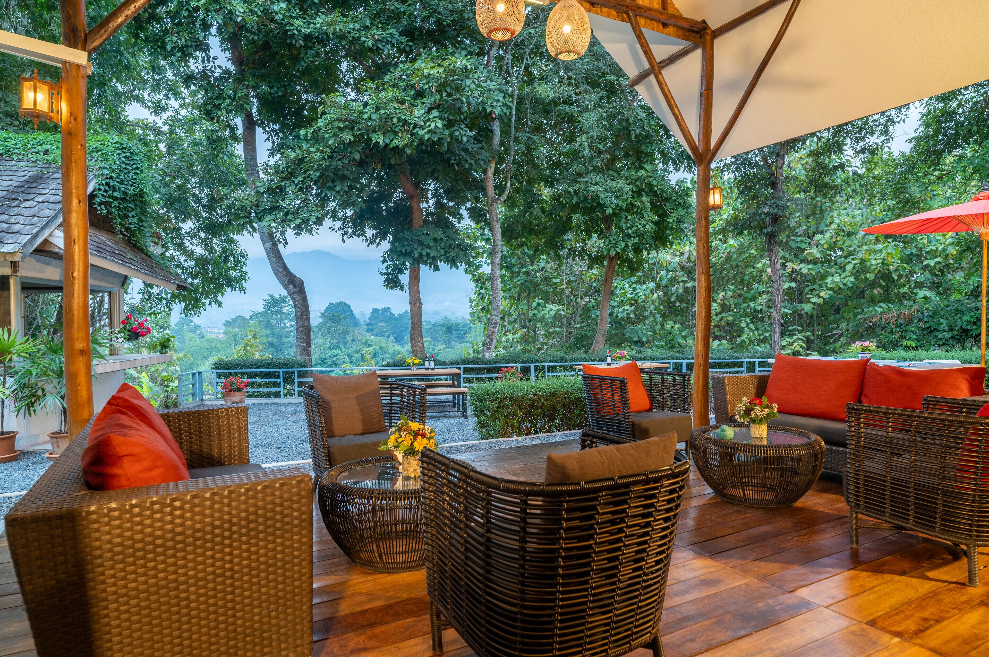 An outdoor seating area with wicker furniture, a wooden deck, and a view of lush greenery and mountains.