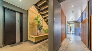 Un hall d’hôtel moderne avec une porte sombre, un escalier, un mur végétal et un mur recouvert de panneaux en bois.