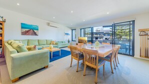 Un salon moderne avec un canapé, une table basse et une table à manger. Un tableau orne le mur et une fenêtre donne sur un immeuble.