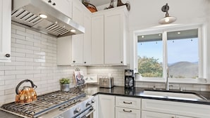 Una cocina con armarios blancos, una estufa, un lavamanos y una ventana con vistas al exterior.