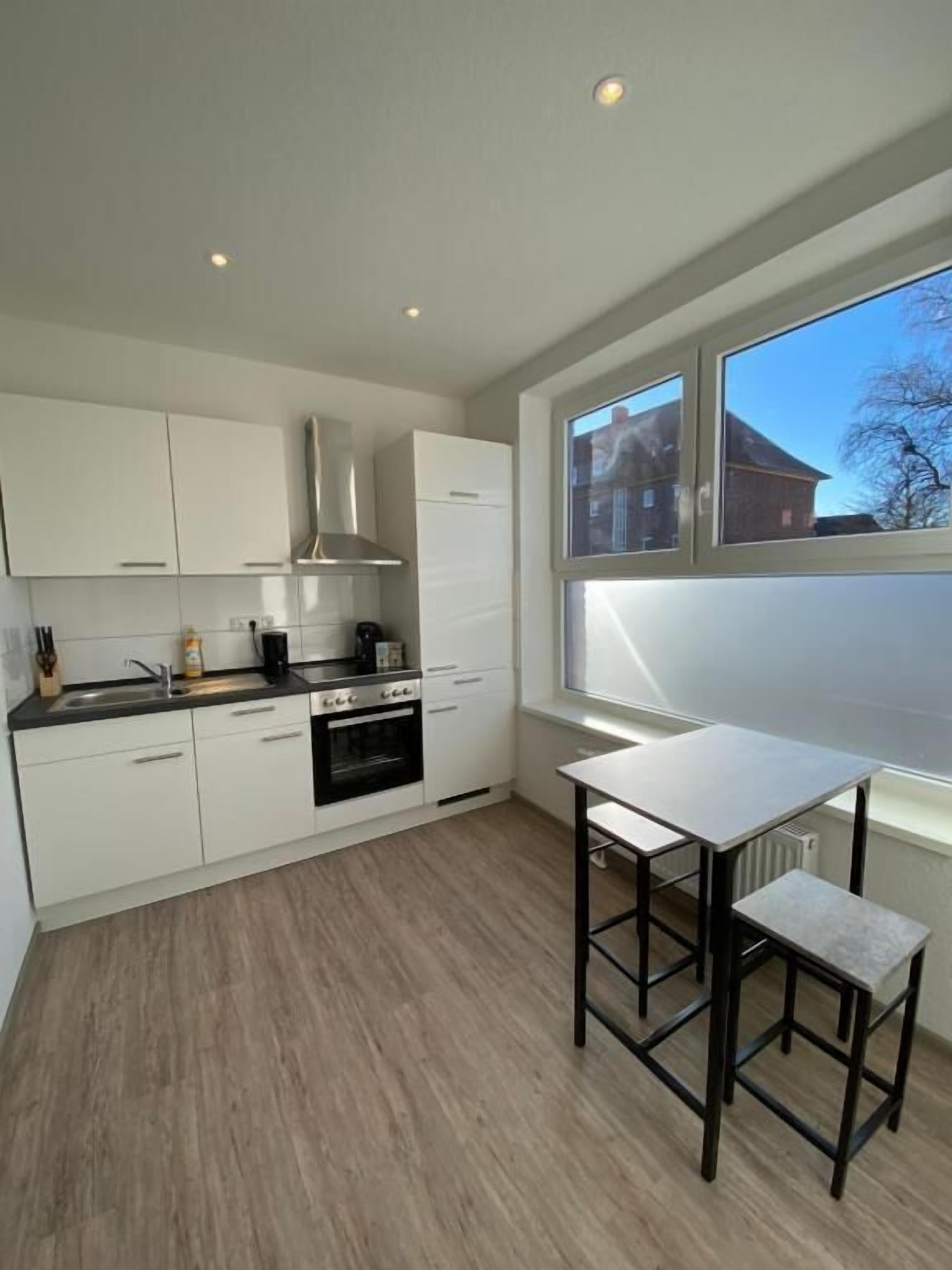 A modern kitchen with white cabinets, a black oven, and a window providing natural light.
