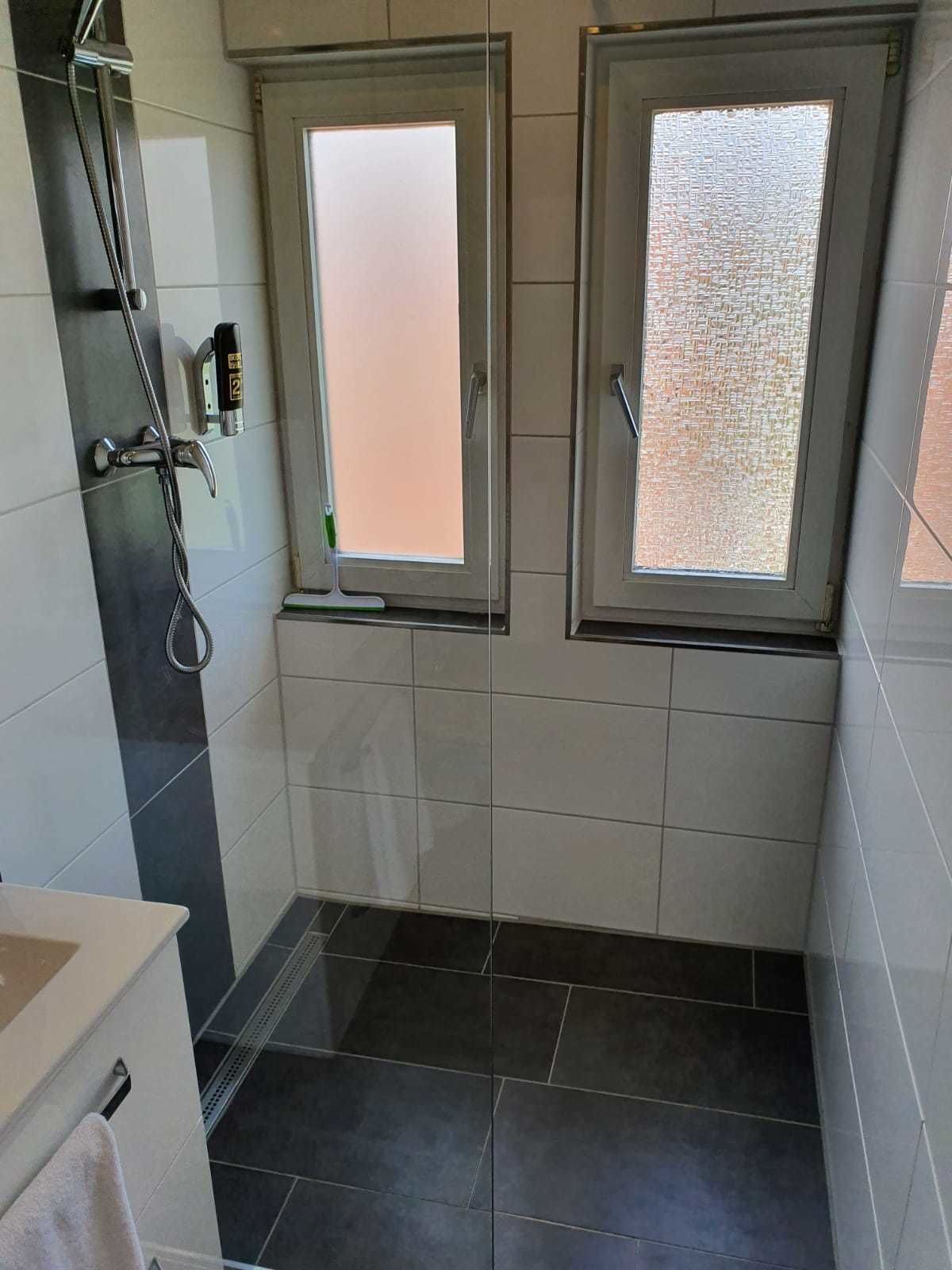 Un baño pequeño con dos ventanas, una ducha y un perchero para toallas.