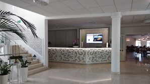 A modern hotel lobby with a reception desk, a staircase with a decorative railing, and a large plant. - Nadodrzański Dwór (Nowa Sól)