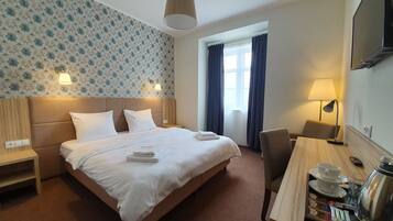 Ein Hotelzimmer mit einem großen Bett, zwei Nachttischlampen, einem Schreibtisch mit Kaffeemaschine und einem an der Wand befestigten Fernseher.