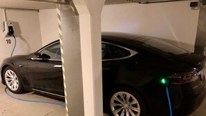A black car parked in a garage with a charging station and a visible number 10 on the wall. - House Hayer - House Hayer Whg 10 (Sankt Peter-Ording)