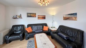 A living room with a black leather sofa set, a coffee table, and wall art depicting landscapes and a lighthouse. - House Hayer - House Hayer Whg 10 (Sankt Peter-Ording)