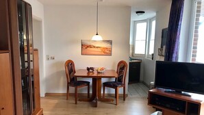 A compact living space with a dining table, two chairs, a television on a stand, and a cabinet. - House Hayer - House Hayer Whg 10 (Sankt Peter-Ording)