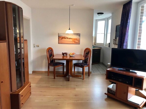 A compact living space with a dining table, two chairs, a television on a stand, and a cabinet.