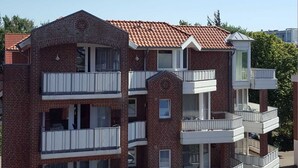 A multi-story brick building with balconies, a red-tiled roof, and a clear sky. - House Hayer - House Hayer Whg 10 (Sankt Peter-Ording)