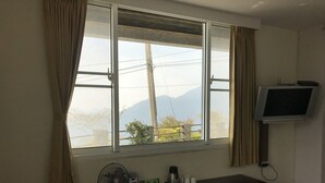 A room with a large window, a flat-screen TV mounted on the wall, a desk with a fan, and a coffee maker. - Zhu Yuan Homestay (Zhuqi)