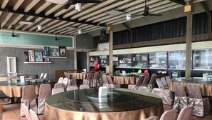 A restaurant with round tables and cushioned chairs, a high ceiling with exposed beams, and a kitchen area visible through the windows. - Zhu Yuan Homestay (Zhuqi)