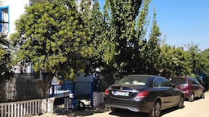 A parking area with two cars, a blue gate, and a building with a white facade and blue trim.