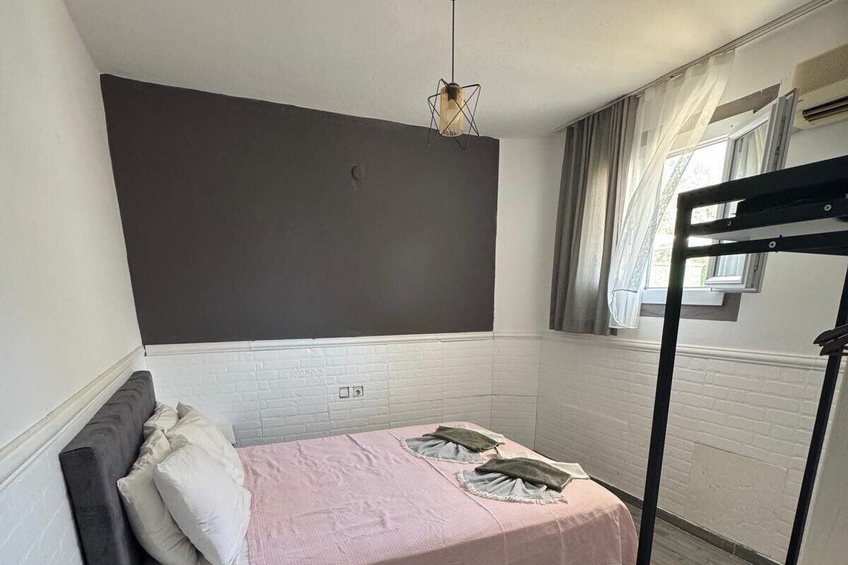 A single bed with a pink bedspread, a black headboard, and a white brick-patterned wall.