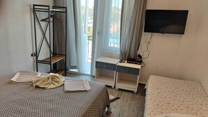 A bedroom with a bed, a desk, a TV, and a window with curtains.