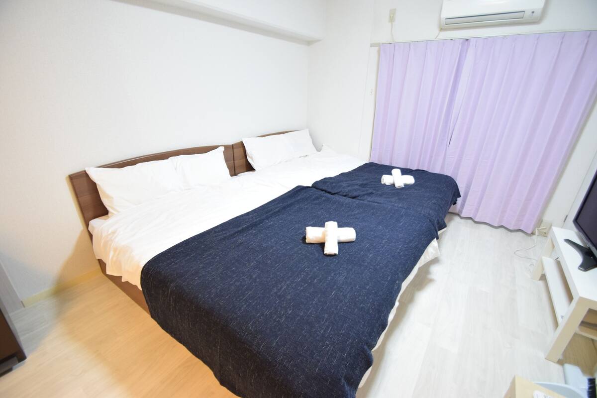 A hotel room with a bed, a desk, and an air conditioning unit.