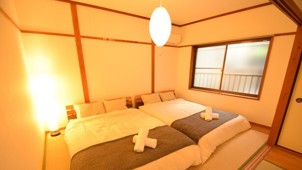 Une chambre de style japonais traditionnel, avec un sol recouvert de tatamis, un grand lit doté de nombreux oreillers et une fenêtre coulissante à panneaux de shoji.