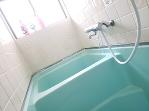 A bathroom with a bathtub, a shower, and a window with bottles on the sill. - Color Ebie (Osaka)