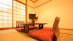 Une pièce de style japonais traditionnel, avec un sol recouvert de tatamis, une table basse, des chaises en bois et un téléviseur.