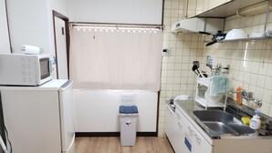 Une cuisine compacte équipée d’un four à micro-ondes, d’une petite poubelle, d’un évier avec un robinet et d’une fenêtre avec un rideau.