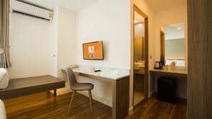 Habitación de hotel con un escritorio de madera, una silla, una cama, un baño con lavabo y espejo, y un televisor mostrando 'B2'.
