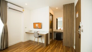 Habitación de hotel con piso de madera, un escritorio con silla, televisor montado en la pared, una puerta con espejo y un cesto de basura pequeño.