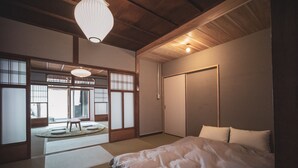 A traditional Japanese-style bedroom with tatami flooring, a low wooden bed, and sliding doors leading to a balcony. - Modern Machiya MIBU (Kyoto)