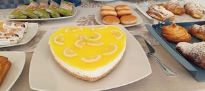 A dessert table with a heart-shaped cheesecake topped with lemon slices, surrounded by various pastries and bread. - Bed & Breakfast Plaza (Lampedusa)