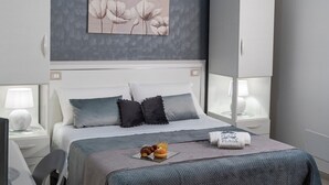 Un dormitorio moderno con una cama grande, una obra de arte gris en la pared y una mesita de noche con lámpara.