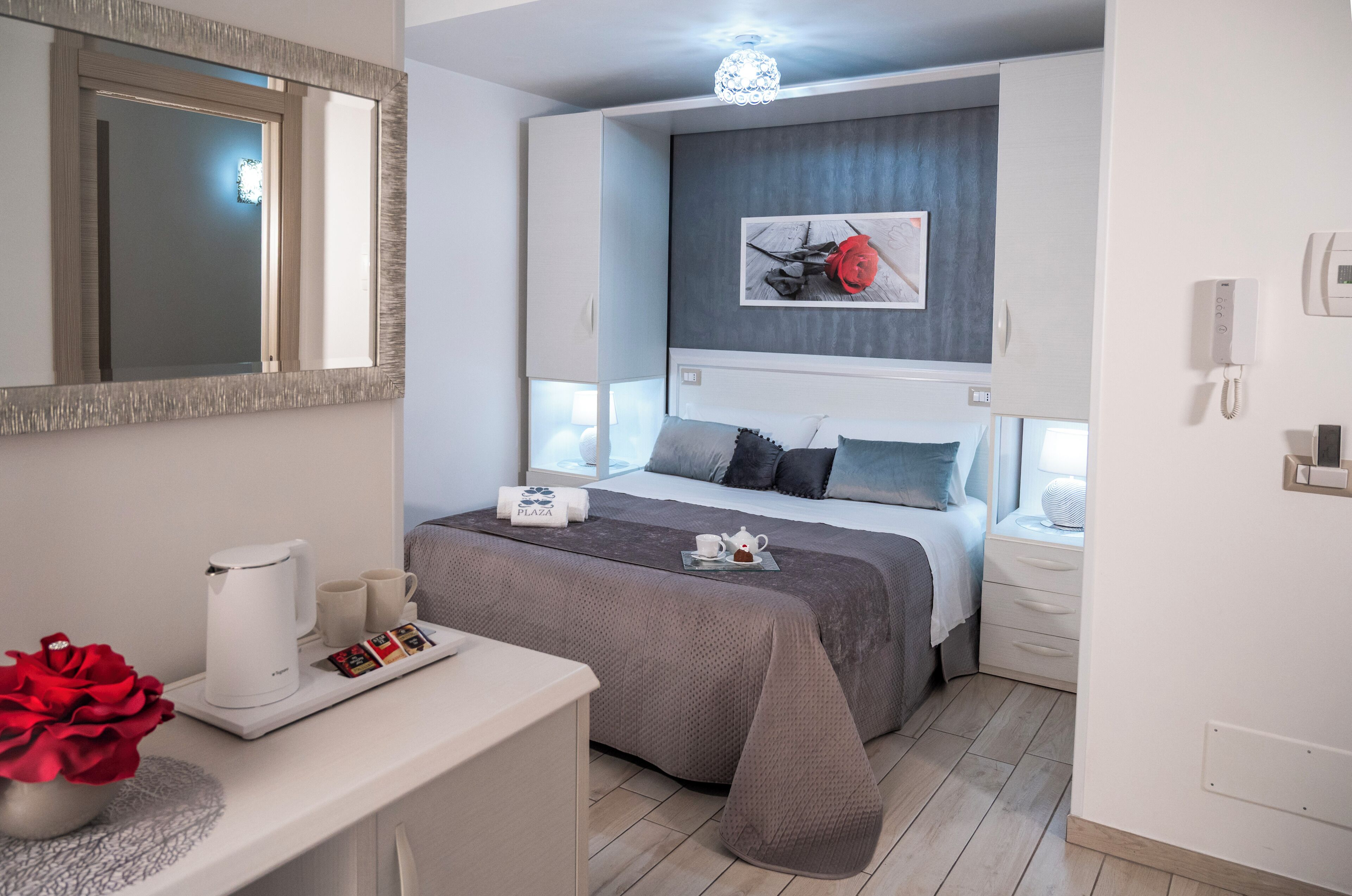 Ett modernt hotellrum med en stor säng, sängbord, ett skrivbord med en kaffebryggare och tekanna samt en dekorativ spegel.