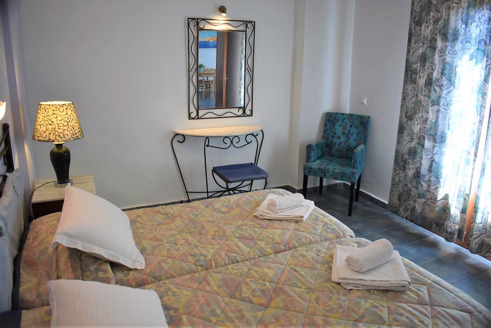 Habitación de hotel con cama, una silla, un escritorio con lámpara y un espejo en la pared.