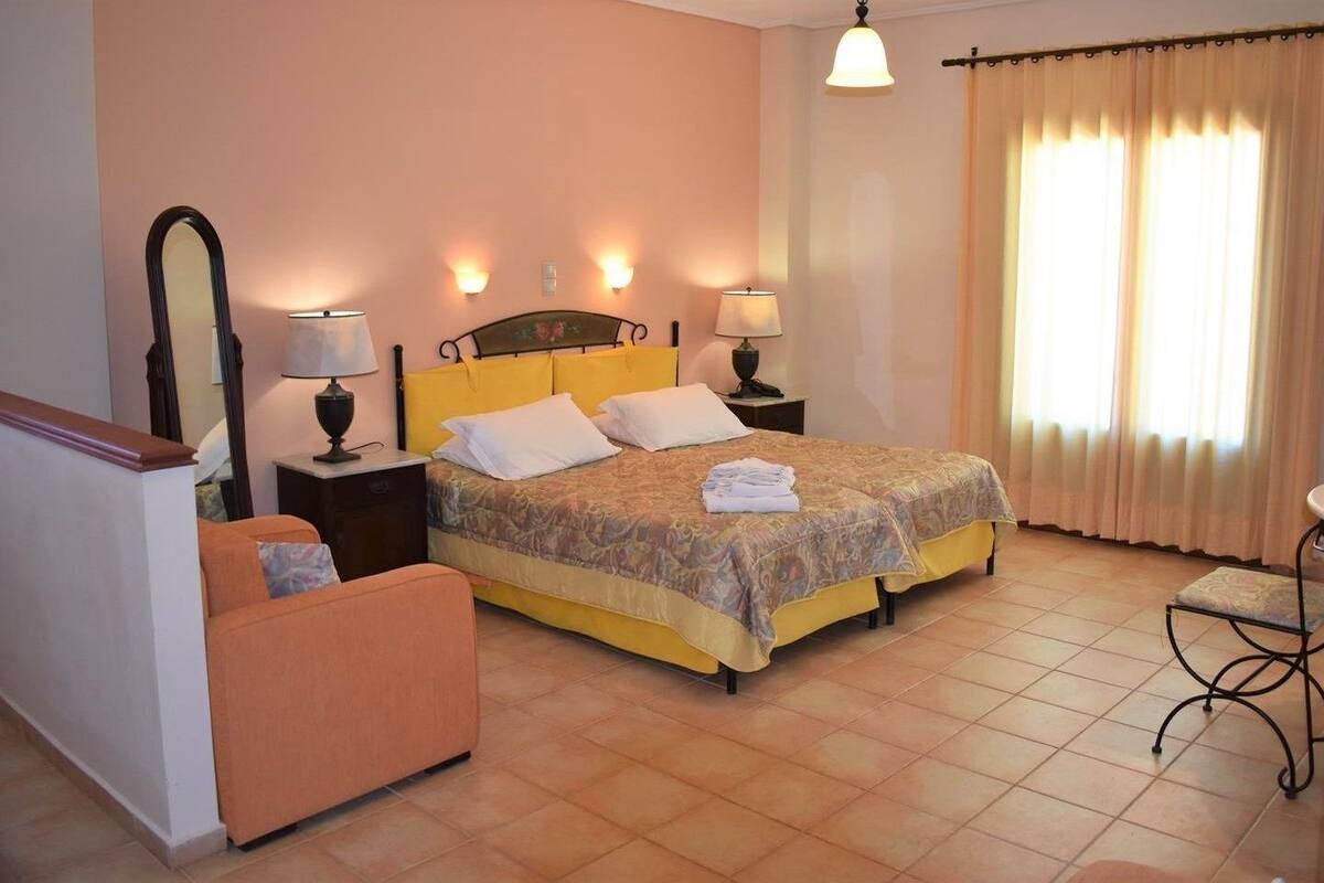 A hotel room with a bed, two bedside tables with lamps, a chair, a small table, and a window with curtains.