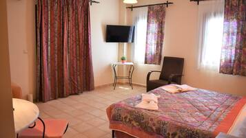 A hotel room with a bed, a chair, a small table with a plant, and a television on the wall.