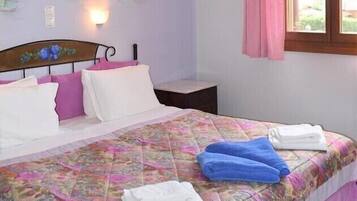 Un dormitorio con cama, almohadas, una mesita de noche, una lámpara de pared y una ventana con cortinas.