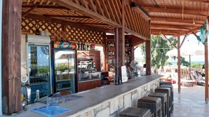 A covered outdoor bar area with a wooden ceiling, a refrigerator, a coffee machine, and a variety of bottles. - Melidron Hotel (Kefalonia)