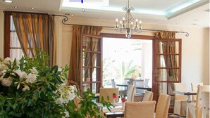 A dining area with a chandelier, checkered floor, and curtains. - Melidron Hotel (Kefalonia)