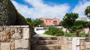 A stone staircase leading to a pink house with a tiled roof, surrounded by greenery and a clear sky. - Melidron Hotel (Kefalonia)