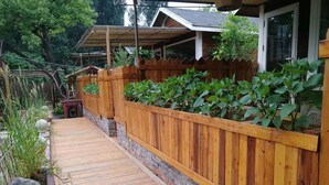 Una terraza de madera con un muro de ladrillo y una valla de madera, rodeada de follaje.
