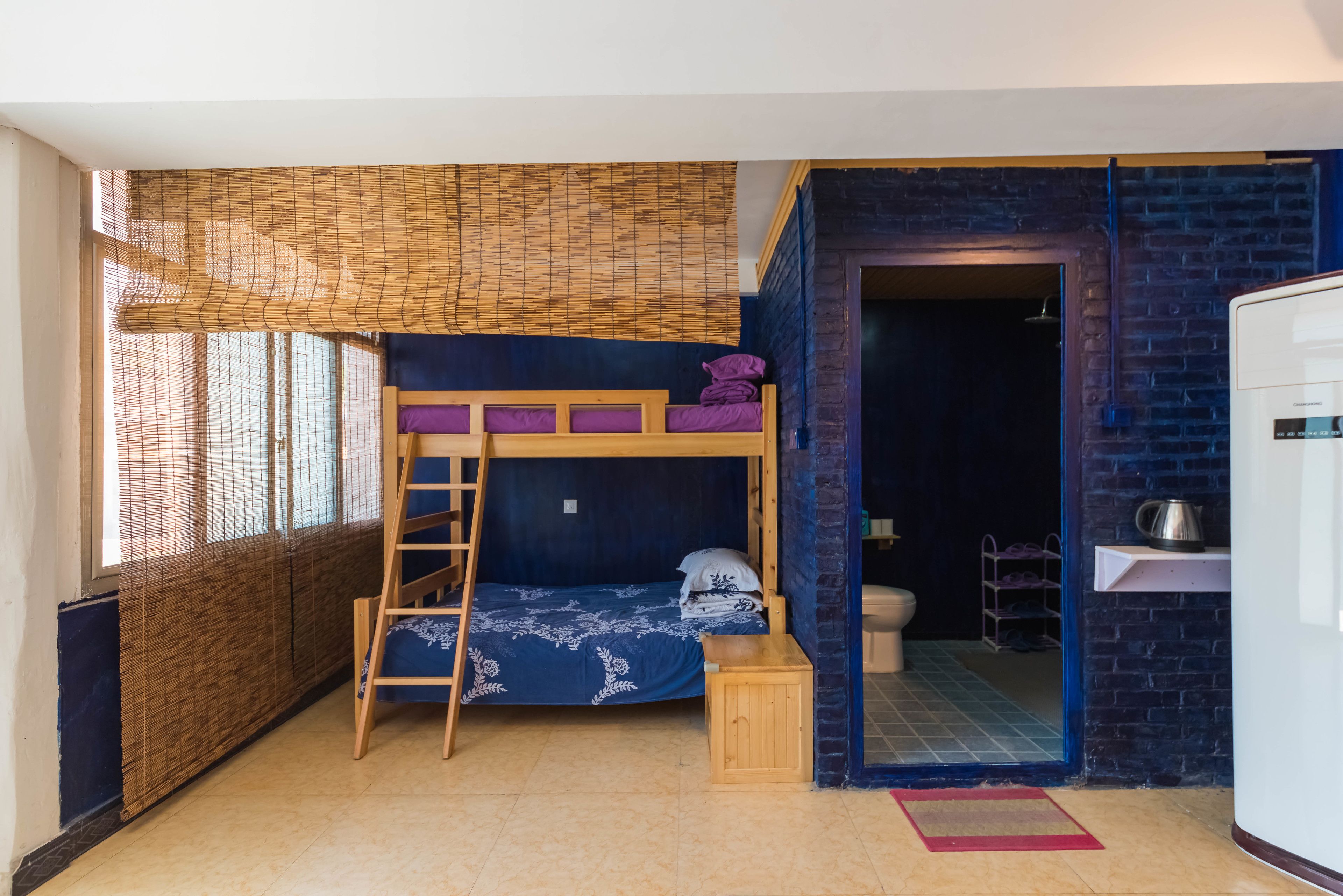 Habitación pequeña con literas, un taburete de madera, una escalera, inodoro y una zona de kitchenette.