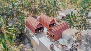 A small, rustic building with a red roof, surrounded by lush greenery and palm trees. - Sukawati Inn (Penida Island)