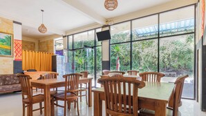 A spacious dining area with wooden tables and chairs, large windows offering a view of greenery outside. - Sukawati Inn (Penida Island)