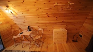 A wooden cabin with a small table, two chairs, a kettle, and a chest of drawers.