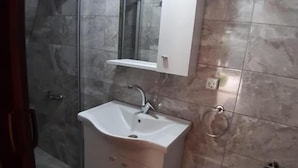 A bathroom with a white sink, a mirror above it, a shower, and a toilet.