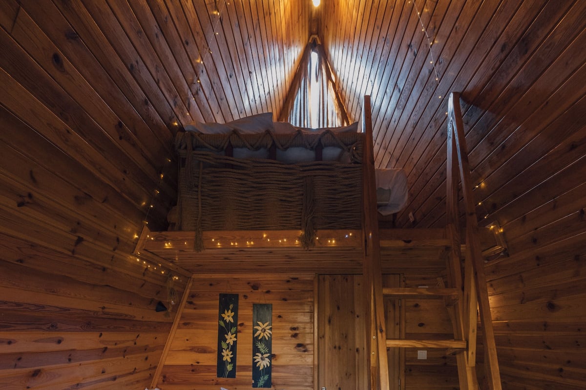 Een knus slaapkamer in een houten chalet, met een hoogslaper, een houten trapje en een klein houten tafeltje.