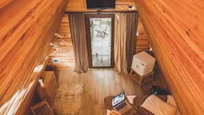 A cozy cabin interior with a bed, a desk, a chair, and a window.