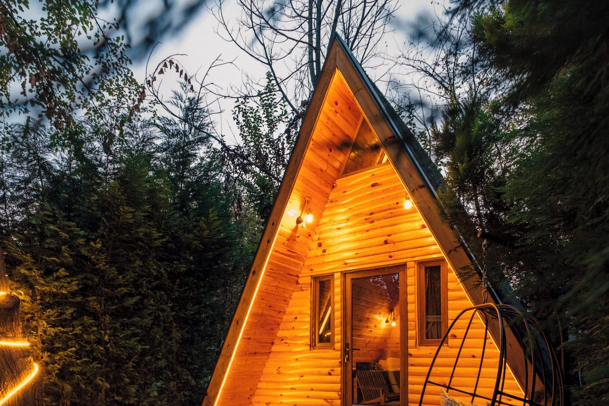 Een houten chalet met een bubbelbad en een hangstoel op een houten terras, omringd door bomen.