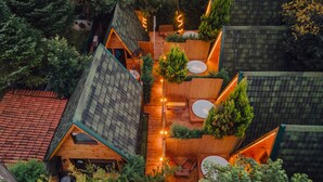A modern, multi-level wooden cabin with a sloped roof, surrounded by dense greenery.