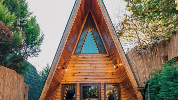 A wooden cabin with a triangular roof, a hot tub, and two rocking chairs.