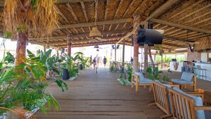Una terraza de madera con techo de paja, asientos exteriores y plantas en macetas.