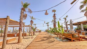 A wooden deck leading to a beach area with palm trees, wooden benches, and umbrellas. - Ayvalık Sea Resort (Ayvalik)