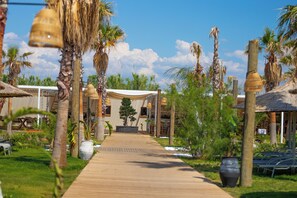 A wooden pathway leading to a building with a thatched roof, surrounded by palm trees and potted plants. - Ayvalık Sea Resort (Ayvalik)